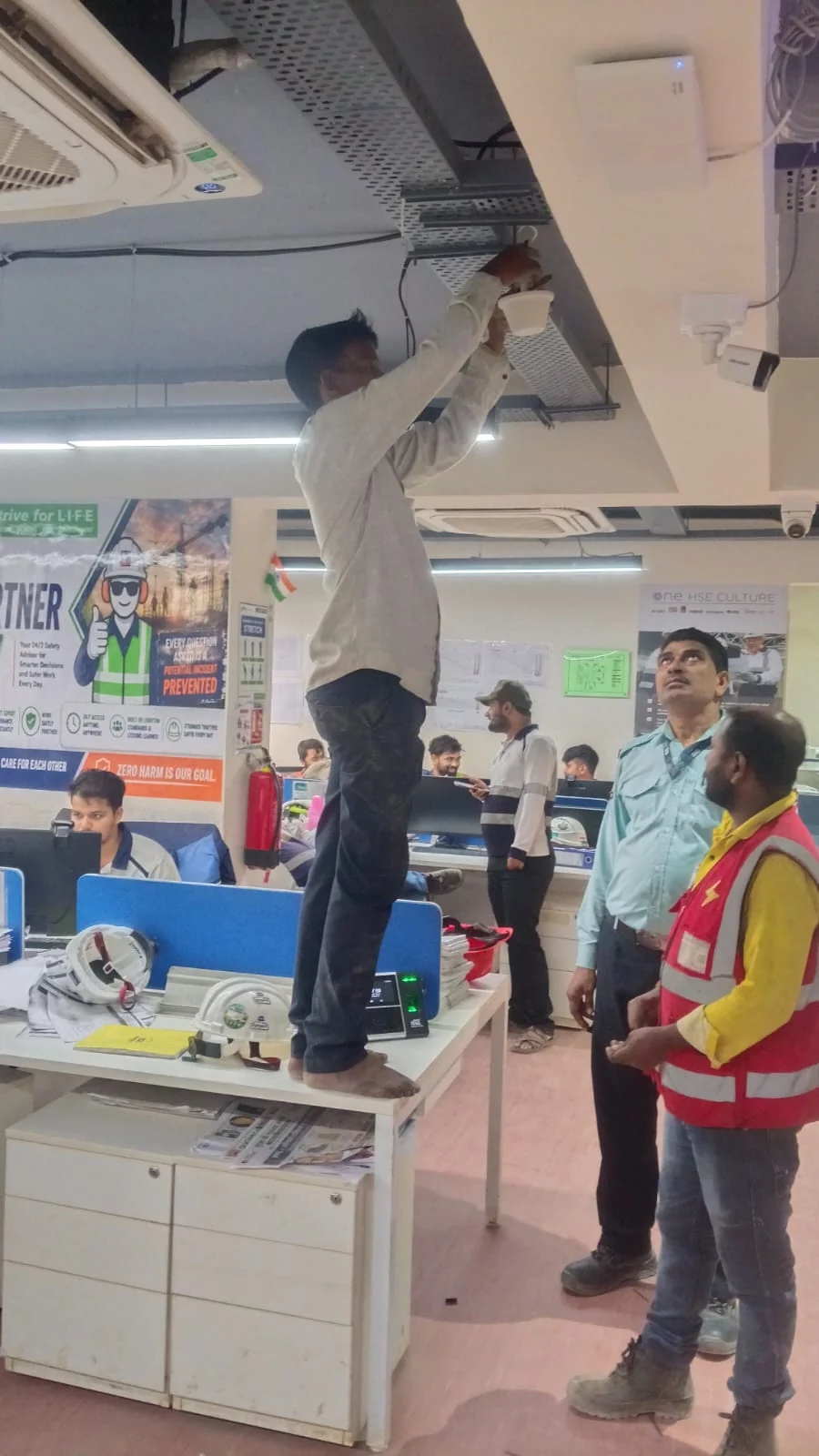 Technician installing signal booster equipment in an office ceiling